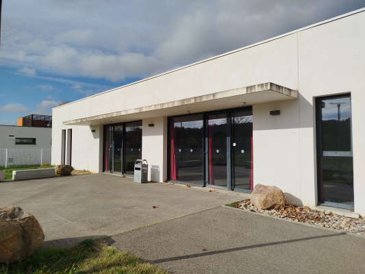 Bâtiment blanc avec grandes baies vitrées et portes, parking et rochers.