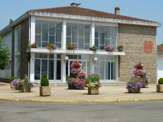Bâtiment avec façade en brique, grandes fenêtres, fleurs en pots et entrée centrale.