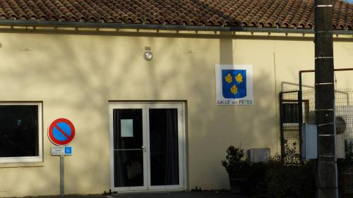 Bâtiment jaune avec porte double, panneau d'interdiction de tourner à gauche, borne de recharge électrique, et drapeau avec inscription.