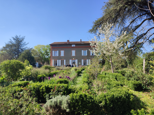Maison à deux étages avec jardin fleuri et arbres.