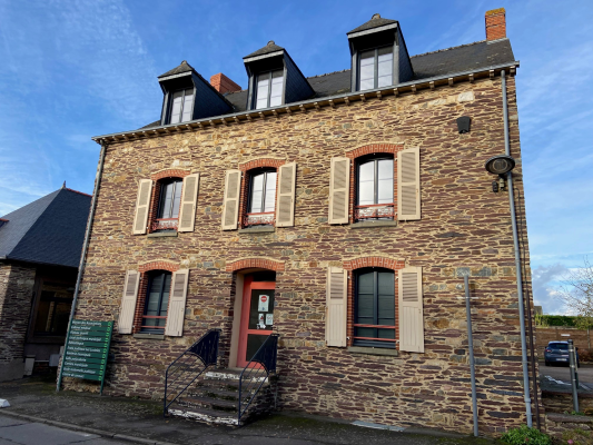 Maison en pierre à deux étages avec fenêtres à volets, porte rouge, et toit mansardé.