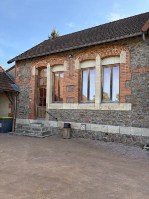 Bâtiment en brique avec grandes fenêtres, escalier extérieur et poubelle.