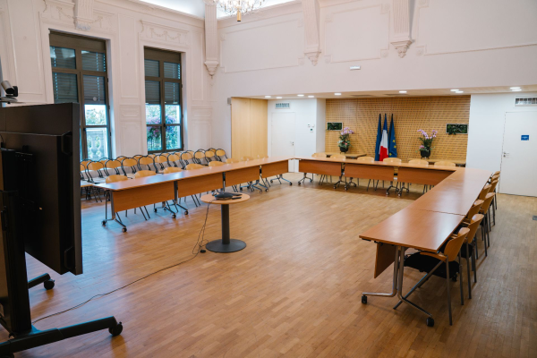 Salle de réunion avec tables, chaises, vidéo projecteur, écran et drapeau.