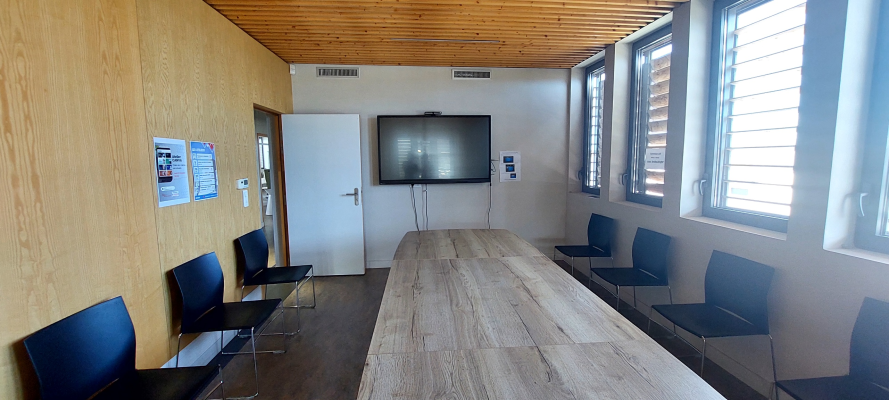 Salle de réunion avec table, chaises, écran et affiches.