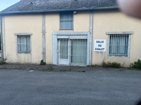 Bâtiment avec trois fenêtres grillagées et une porte centrale. Ensoleillé, devant une route.