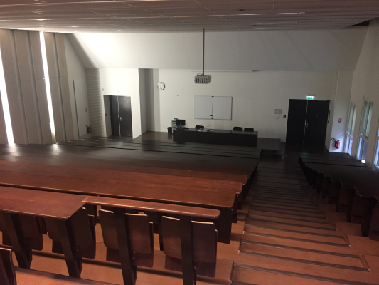 Salle de classe avec tables, chaises, tableau blanc et horloge.