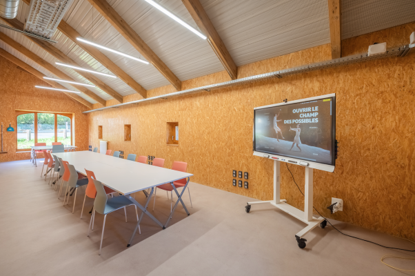 Pièces avec table, chaises, écran, tableau blanc et lumière.