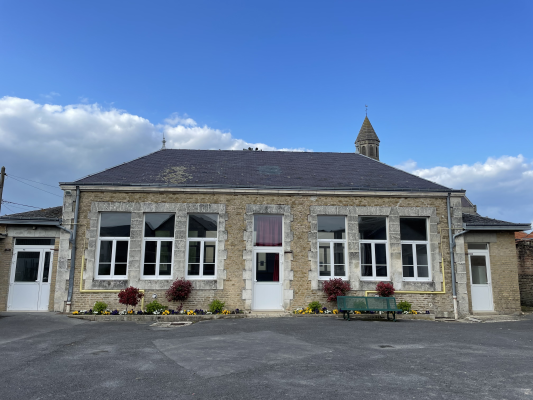 École en pierre avec fenêtres, portes, toit, et un clocher. Cour avec banc et fleurs.