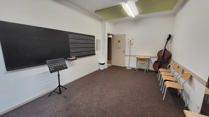 Salle de musique avec tableau, pupitre, chaises, bureau et instrument.
