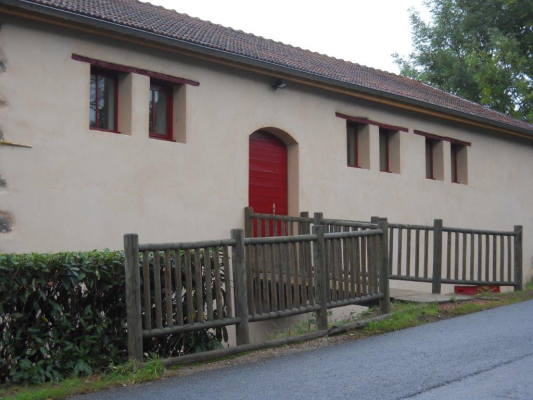 Bâtiment avec porte rouge, fenêtres et clôture en bois le long de la route.