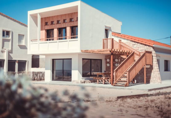 Maison moderne avec escalier extérieur en bois, grandes fenêtres et terrasse.