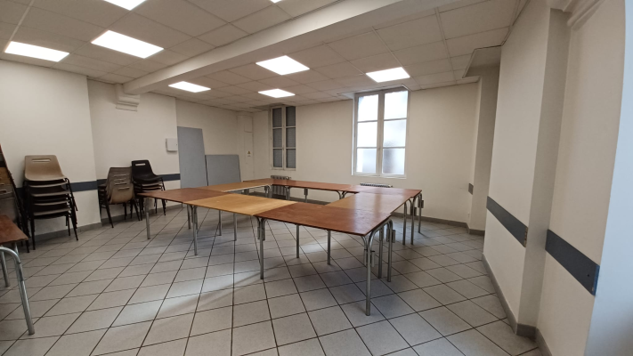 Salle avec tables, chaises, fenêtres et éclairage au plafond.