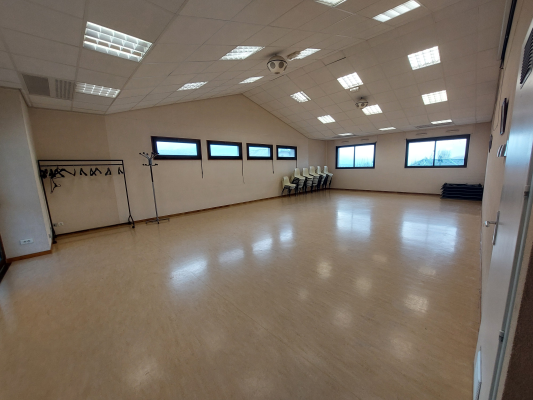 Salle avec sol en bois, bancs, fenêtres, porte, barre de danse et miroir.
