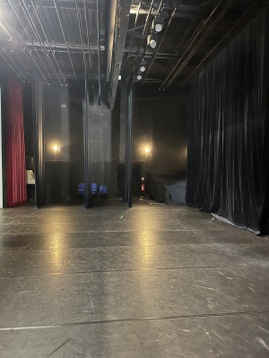 Salle vide avec rideaux, projecteurs et bancs.