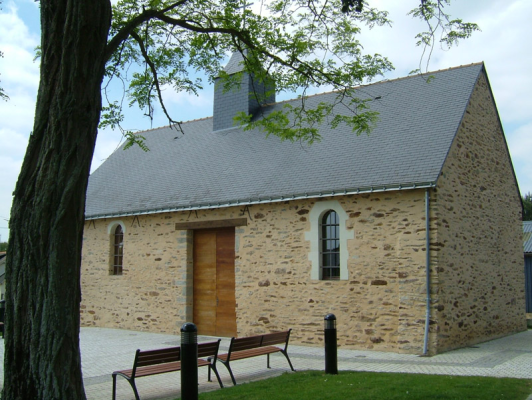 Bâtiment en pierre avec porte en bois, banc et poubelle devant.