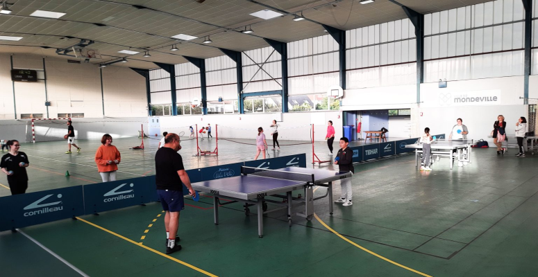 Salle de sport avec tables de ping-pong, filets, ballons, et groupes de personnes.