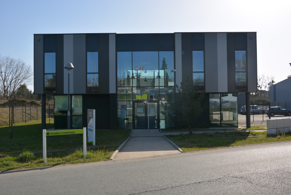 Bâtiment moderne avec façade vitrée, entrée principale, allée et panneaux de signalisation.