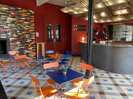 Salle avec tables, chaises, comptoir, et étagères. Mur coloré et sol carrelé.
