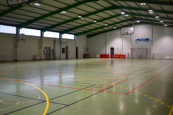 Salle de sport avec paniers, enclos de handball, lignes de sol, escaliers, et portes.