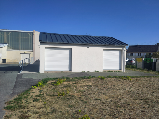 Bâtiment avec deux portes de garage blanches, toit plat, rampes d'accès et terrain herbeux.