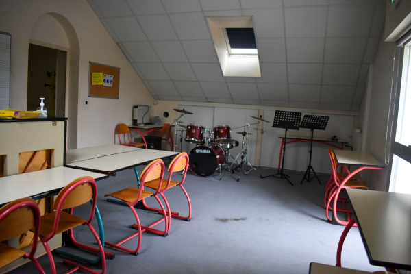Salle de musique avec batterie, pupitres, tables et chaises.