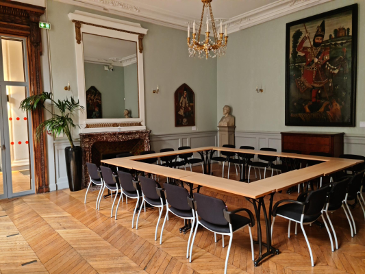 Salle avec table, chaises, lustre, cheminée, plantes, tableaux.