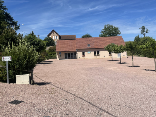 Parking avec gravier, bâtiments, arbres et panneau.